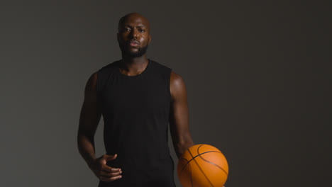 Studio-Portrait-Shot-Of-Male-Basketball-Player-Holding-Ball-Under-Arm-Against-Dark-Background-1